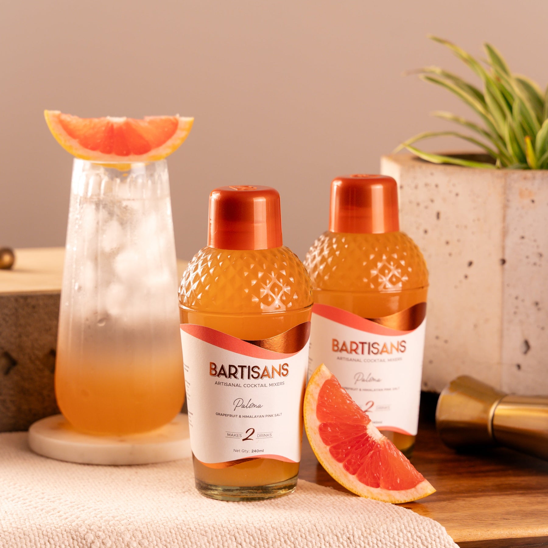 Two bottles of Bartisans cocktail mixers with a cocktail and grapefruit on a wooden surface.