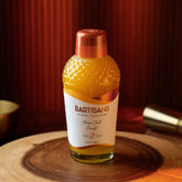 Bottle of BARTISANS cocktail mixer on a wooden surface with a red curtain background
