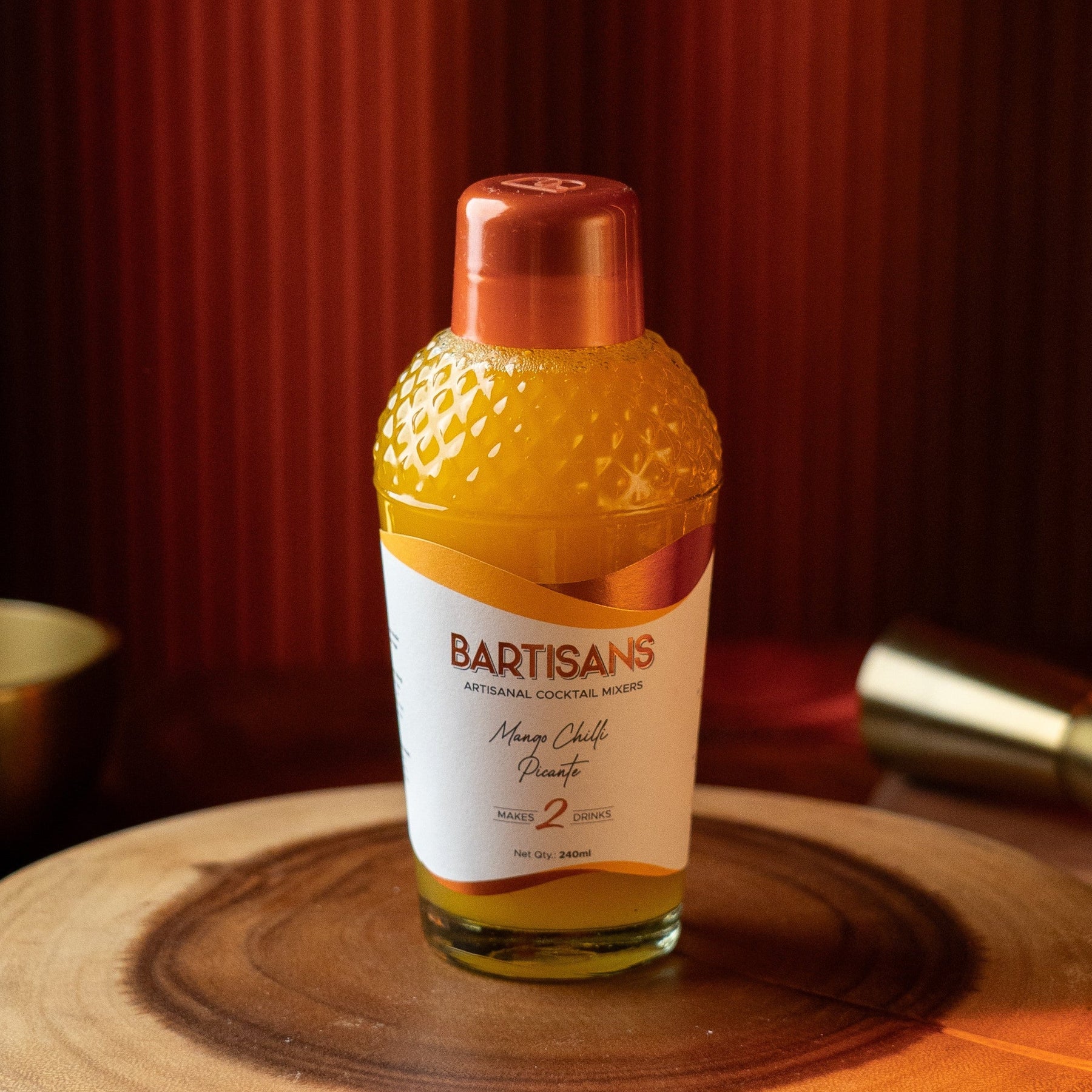 Bottle of BARTISANS cocktail mixer on a wooden surface with a red curtain background