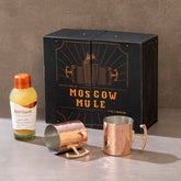 Moscow Mule kit with bottle, mugs, and packaging on a gray surface.