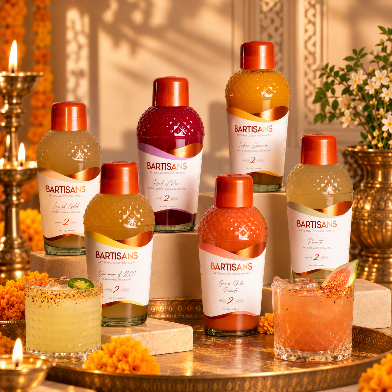 Bartisans artisanal cocktail mixers in assorted flavors displayed with two colorful cocktails, fresh fruit garnishes, orange marigolds, brass trays, and glowing oil lamps in a festive Diwali-inspired setting.