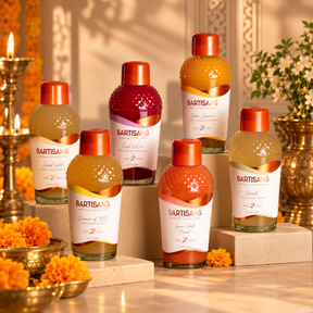 Bartisans artisanal cocktail mixers in assorted flavors displayed on stone pedestals, styled with orange marigolds, brass oil lamps, and warm festive Indian décor.